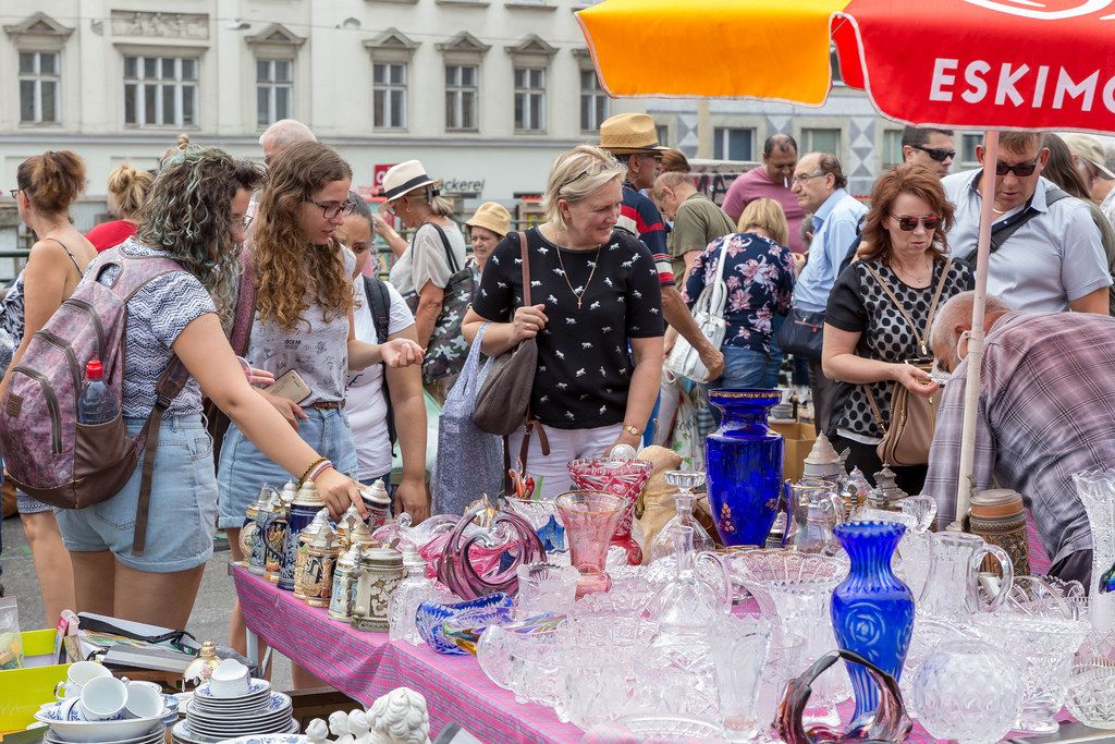 Flohmarkt-Besucher schauen sich Keramikgeschirr und Kristallgeschirr an einem Stand am Naschmarkt an