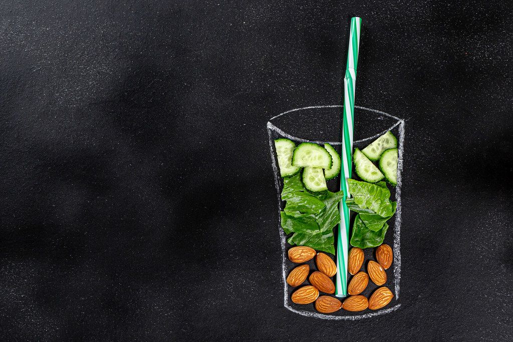 Food ingredients for blending smoothie -cucumbers, lettuce, almonds in painted glass on black chalkboard. Top view with copy space