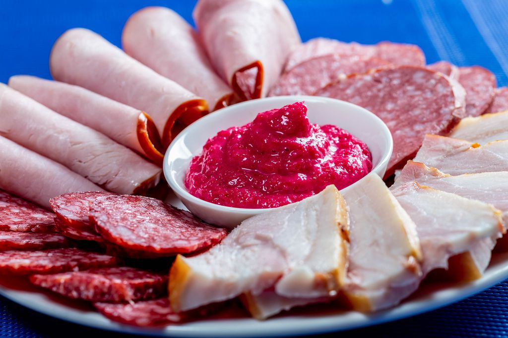 Food tray with delicious salami, pieces of sliced ham, sausage on blue background (Flip 2019)