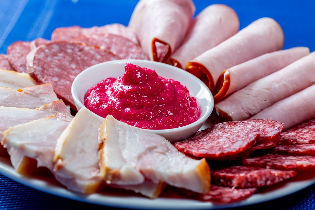 Food tray with delicious salami, pieces of sliced ham, sausage on blue background