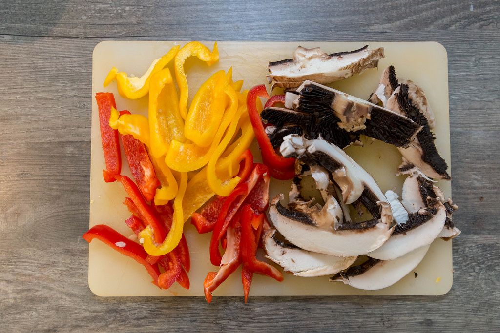 Fresh cut mushrooms with yellow and red pepper slices on a cutting boar - top view