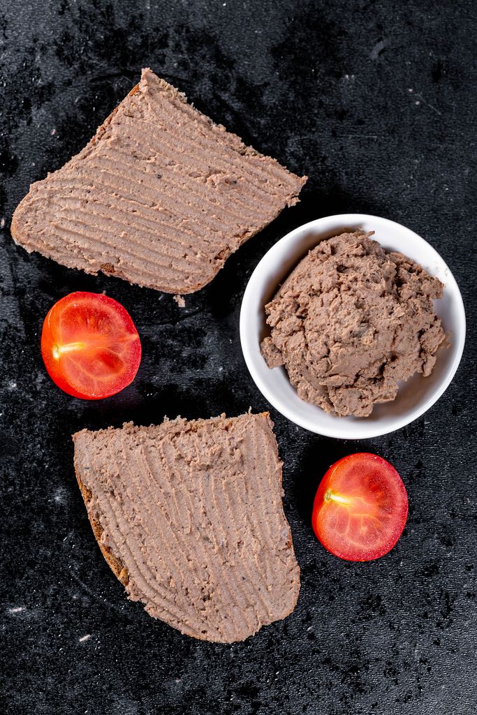 Fresh homemade chicken liver pate on bread over black background