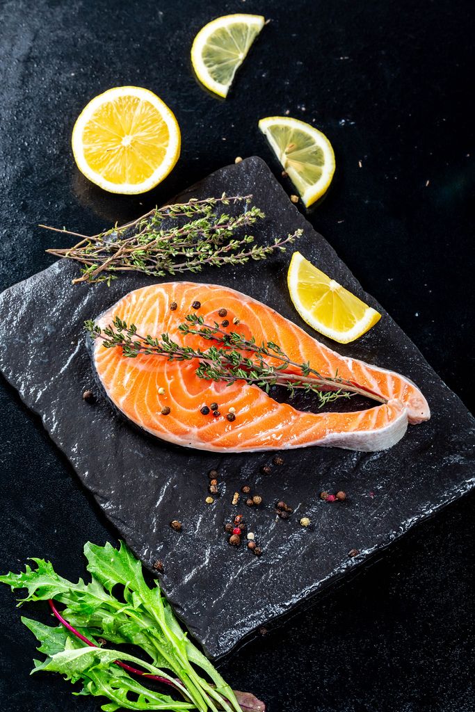 Fresh salmon steak on a black stone tray with spices and lemon slices
