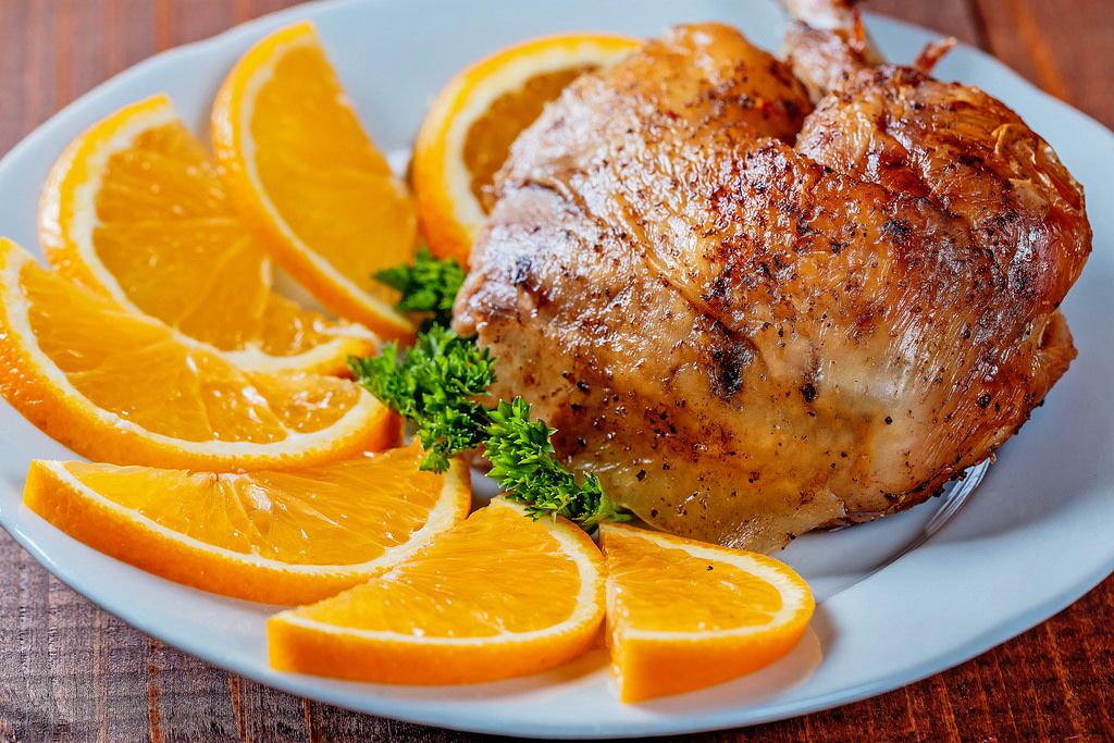Fried duck leg with oranges on a white plate close-up