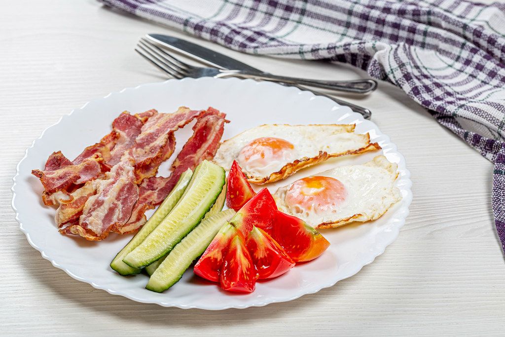 Fried eggs, bacon and pieces of fresh tomatoes and cucumbers. The concept of Breakfast