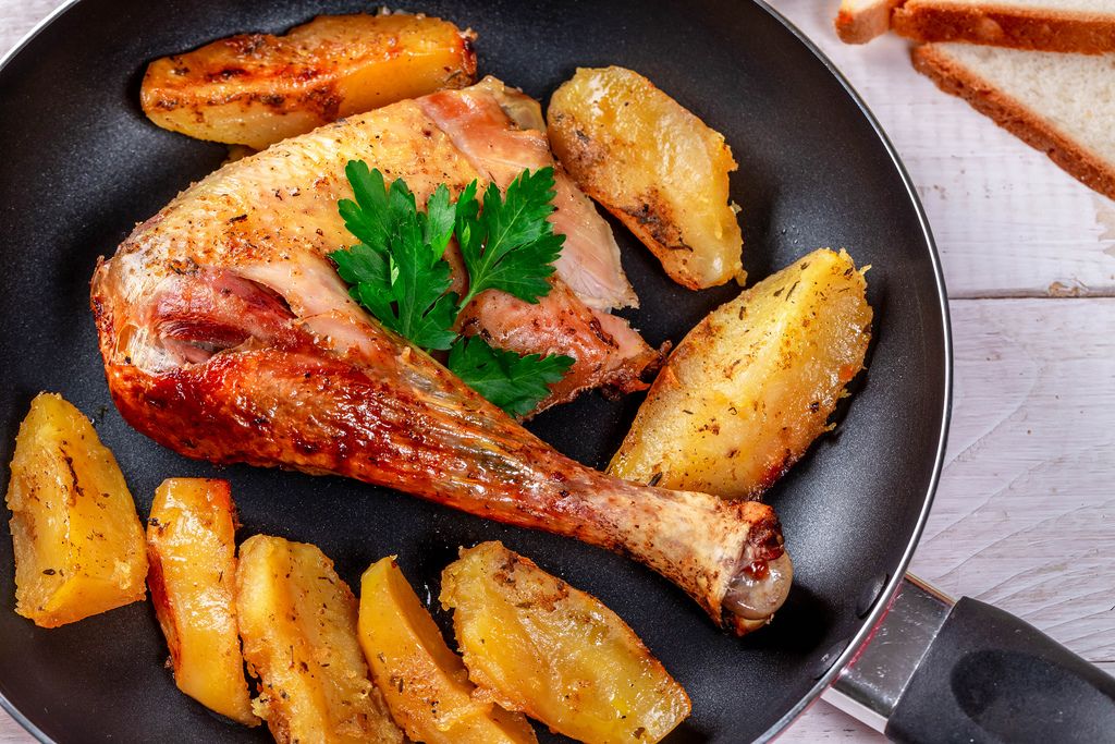 Fried potatoes and chicken leg with parsley in a frying pan