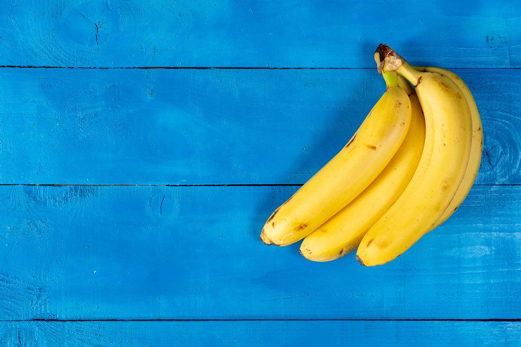 Frische gelbe Bananen auf einem blauen Holzhintergrund, mit freiem ...