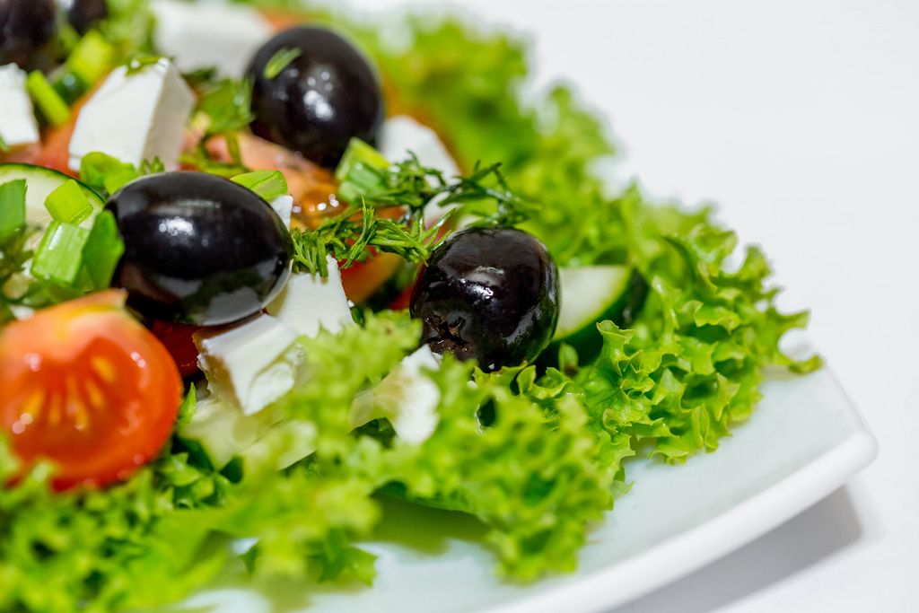 Frischer Diätsalat mit Oliven, Tomaten, Fetakäse und Gurke vor weißem Hintergrund