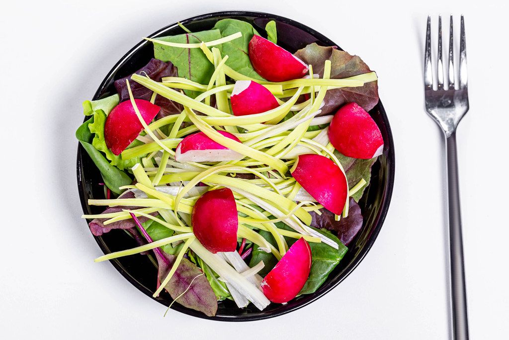 Frischer Salat mit Spinatblättern, Lauch und Radieschen auf einem schwarzen Teller in obene Aufnahme