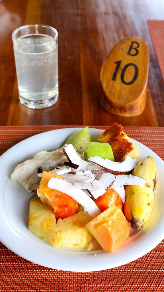 Fruit salad with banana, pineapple, coconut and papaya with a glass of water on orange-red dish pad