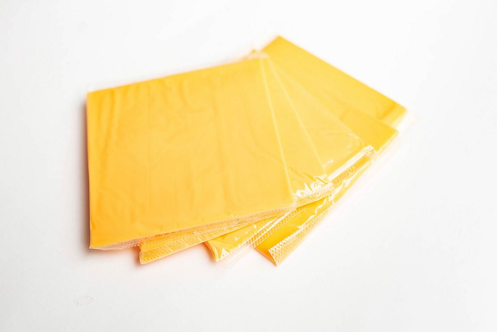 Gelber Scheibenkäse für Sandwich oder Toast in Folie auf weißem Hintergrund