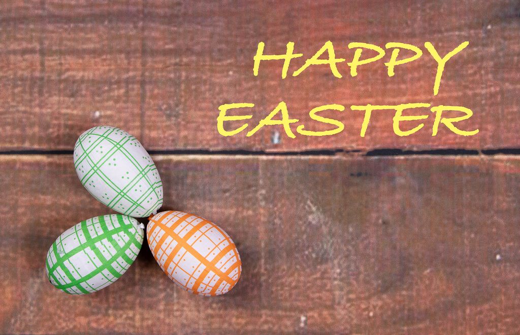 Gelber Text HAPPY EASTER (frohe Ostern) mit drei bemalten Ostereiern auf Holzhintergrund