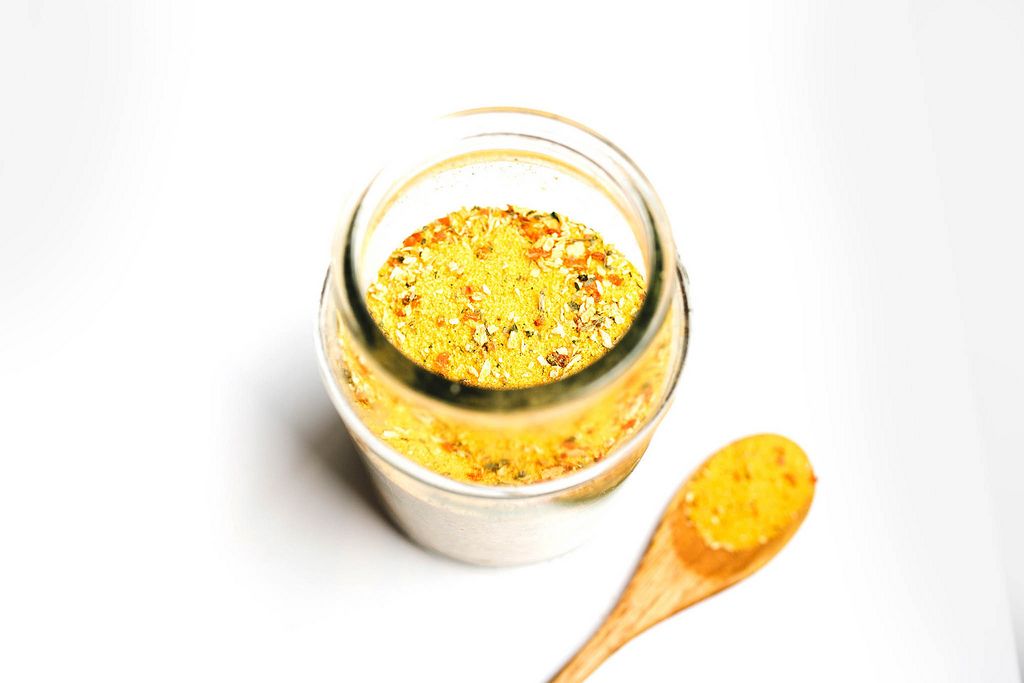 Gelbes Vegeta Gewürz herstellt aus gemahlenen Kräutern und Gemüsesorten in Glas mit hölzernem Löffel