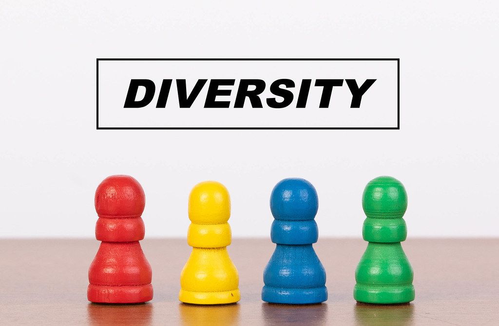 Gerahmter Text DIVERSITY (Vielfalt, Diversität) über vier bunten Spielfiguren auf Holztisch