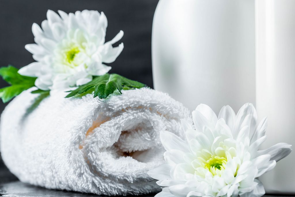 Gerolltes weißes Handtuch dekoriert mit Chrysanthemeblüten vor Kosmetikflaschen