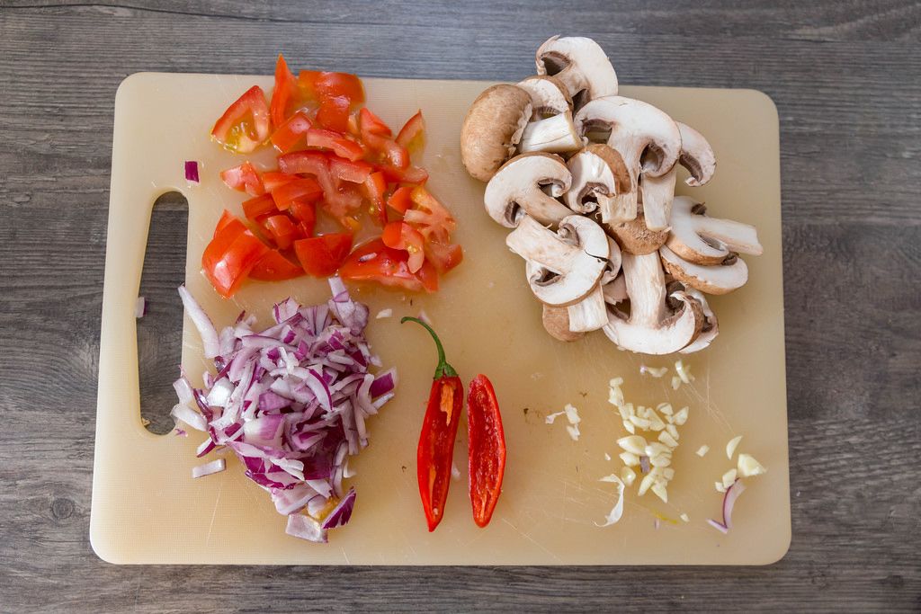 Geschnittenes Gemüse - Tomaten, Pilze, rote Zwiebeln, Chili und Knoblauch auf einem Scheidebrett