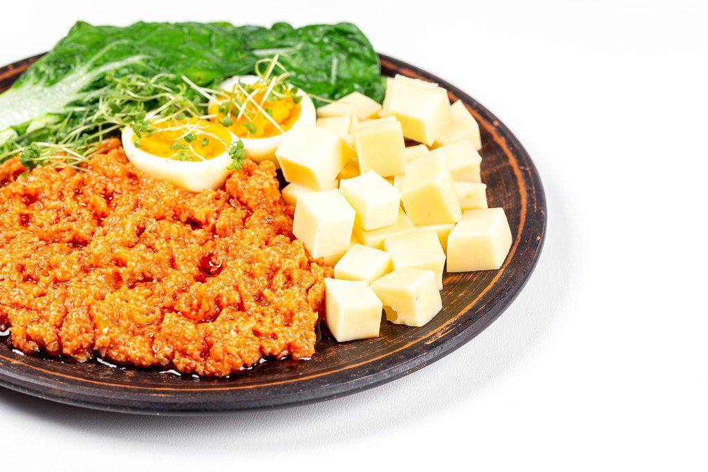 Gesundes Frühstück: Käse, Eier, Gemüse und Zucchinikaviar auf einem Teller vor weißem Hintergrund