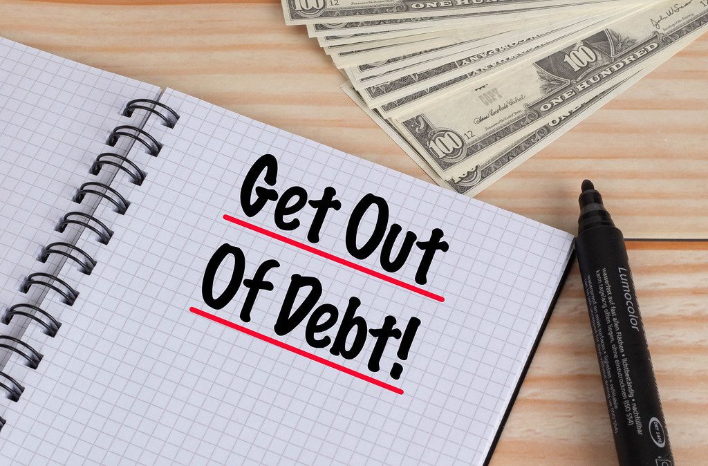 Get out of debt text in notebook and Dollar banknotes on wooden table