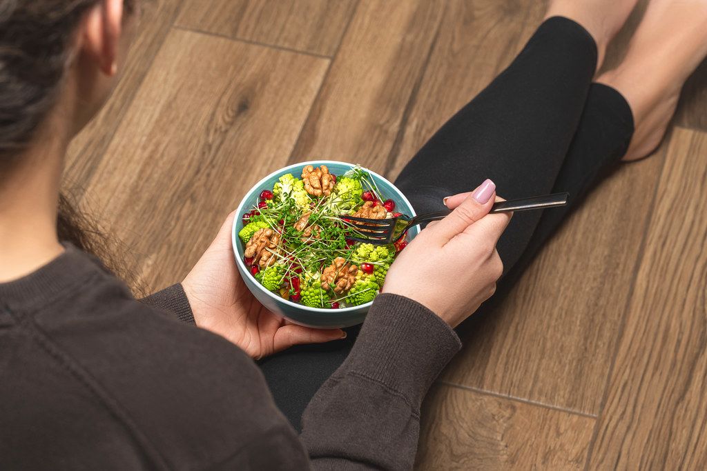 Girl sitting on the floor with a bowl of vegetable salad