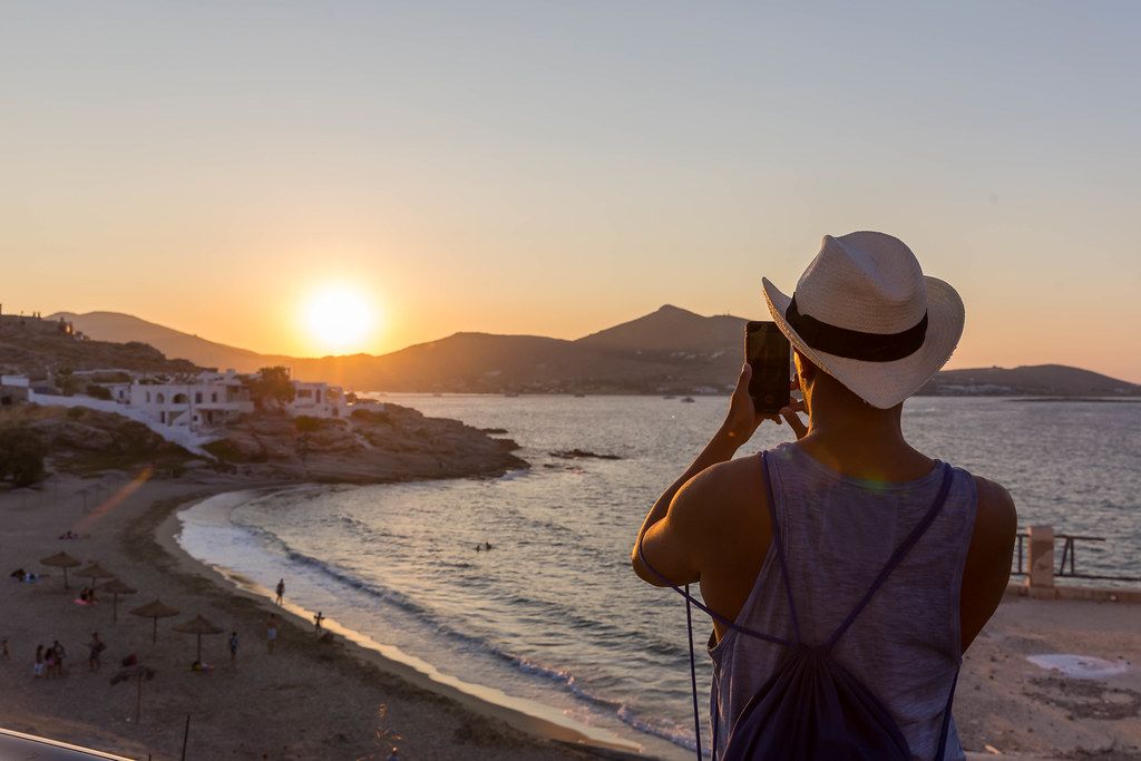 Golden hour - man takes mobile phone photo of the sunset at the coast of the Greek island Paros