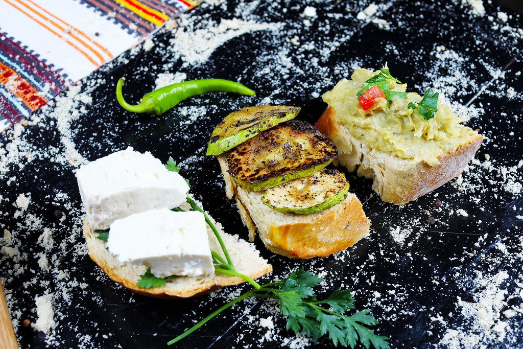 Grilled zucchini slices, eggplant salad and cheese sandwiches on black background