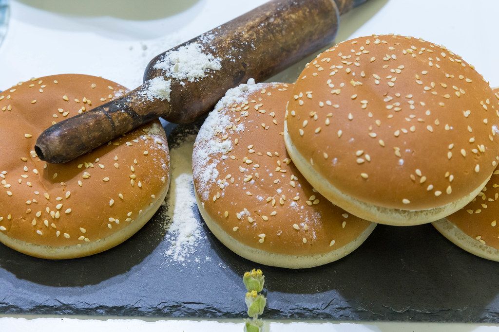 Große Hamburger-Brötchen mit Sesam auf einem schwarzen Brett mit Mehl ...