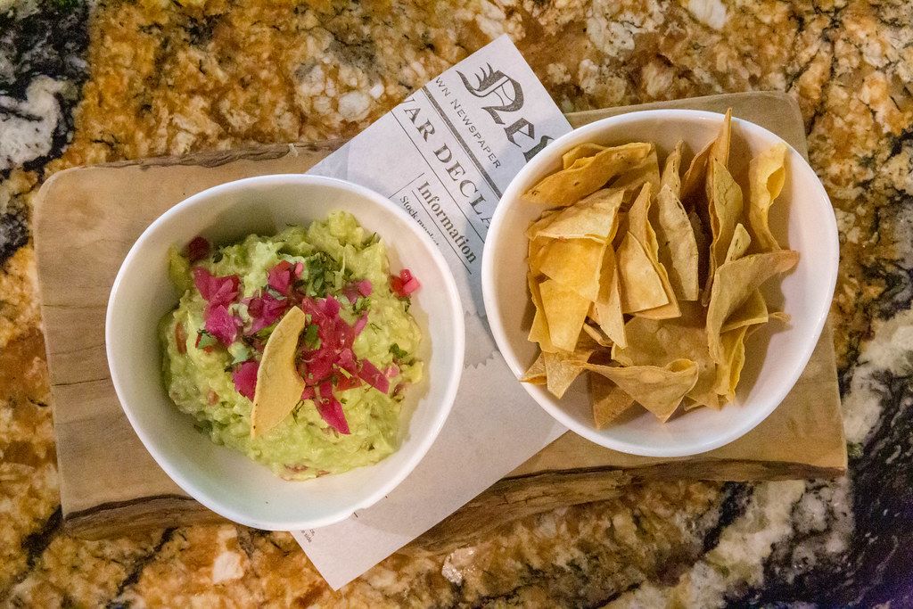 Guacamole made of Avocado, Pico de Gallo and oven baked Tortilla Chips, served on a wooden beam with a Spanish newspaper at Fit Kitchen, Barcelona
