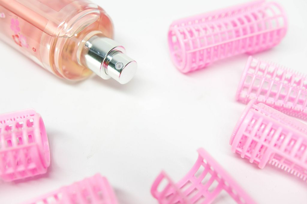 Haarwickler aus Plastik mit einer pinken Parfümflasche auf weißem Untergrund