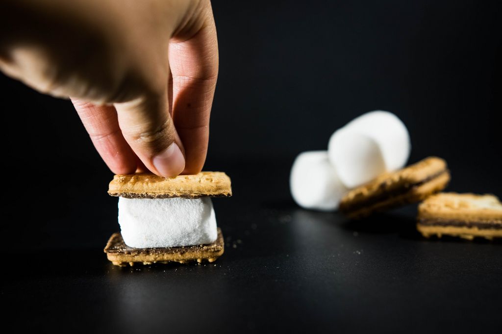 Hand bereitet Smore aus weißem Marshmallow zwischen Keks vor auf schwarzem Hintergrund