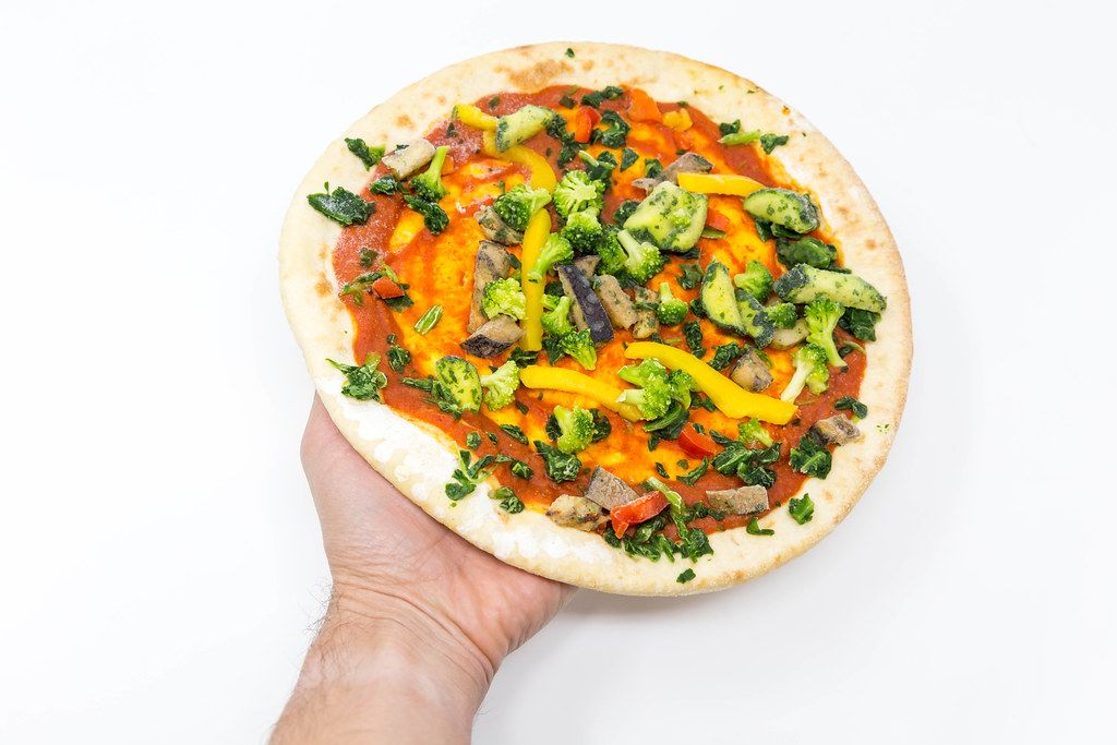 Hand hält eine followfood Verdura Vegan Pizza mit Bio-Dinkelboden vor weißem Hintergrund