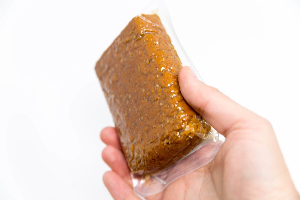 Hand hält eine Packung bio & vegan Räuchertofu Sesam-Mandel von Tukan vor weißem Hintergrund