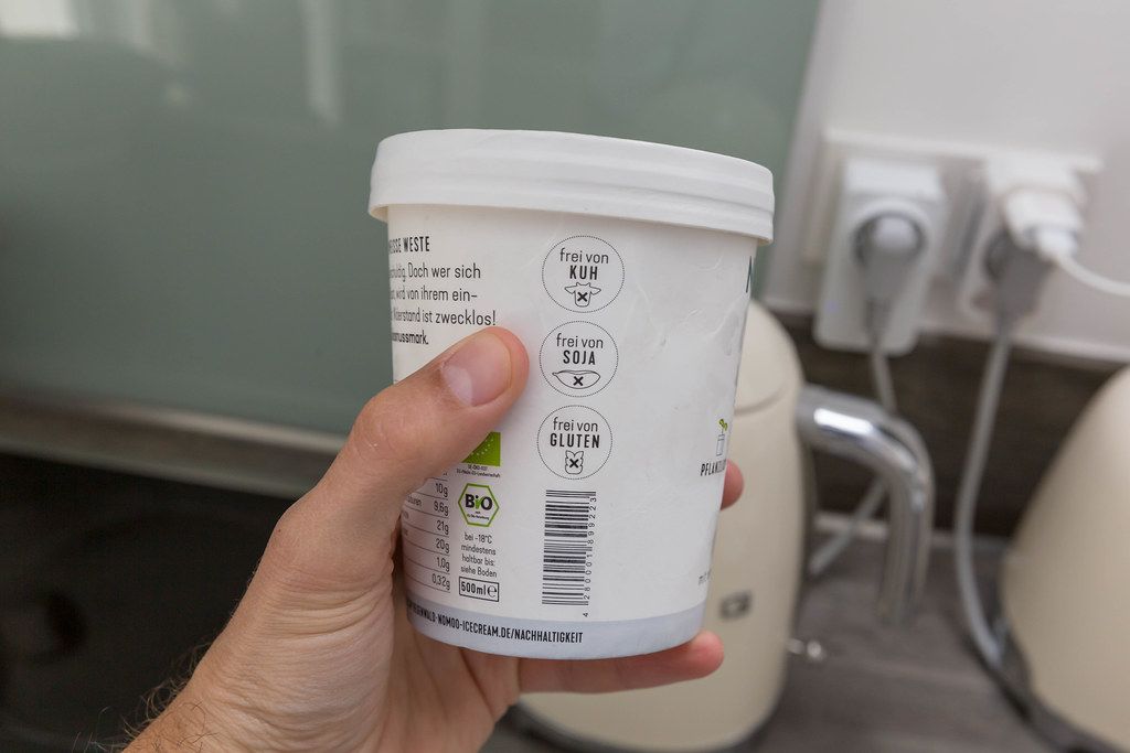 Hand hält Eispackung & zeigt Inhalt des veganen Bio-Eis von Nomoo mit Kokosnuss-Geschmack, frei von Kuhprodukten, Sojafrei und Glutenfrei