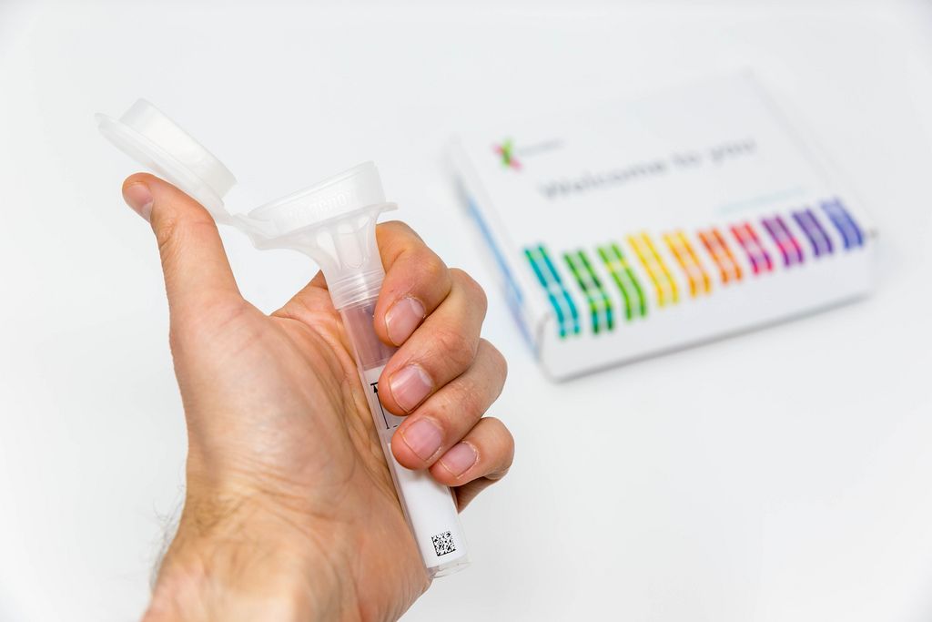 Hand hält Saliva Collection Kit Röhre mit offenem Trichterdeckel von 23andMe zur DNA Analyse - Bestimmung