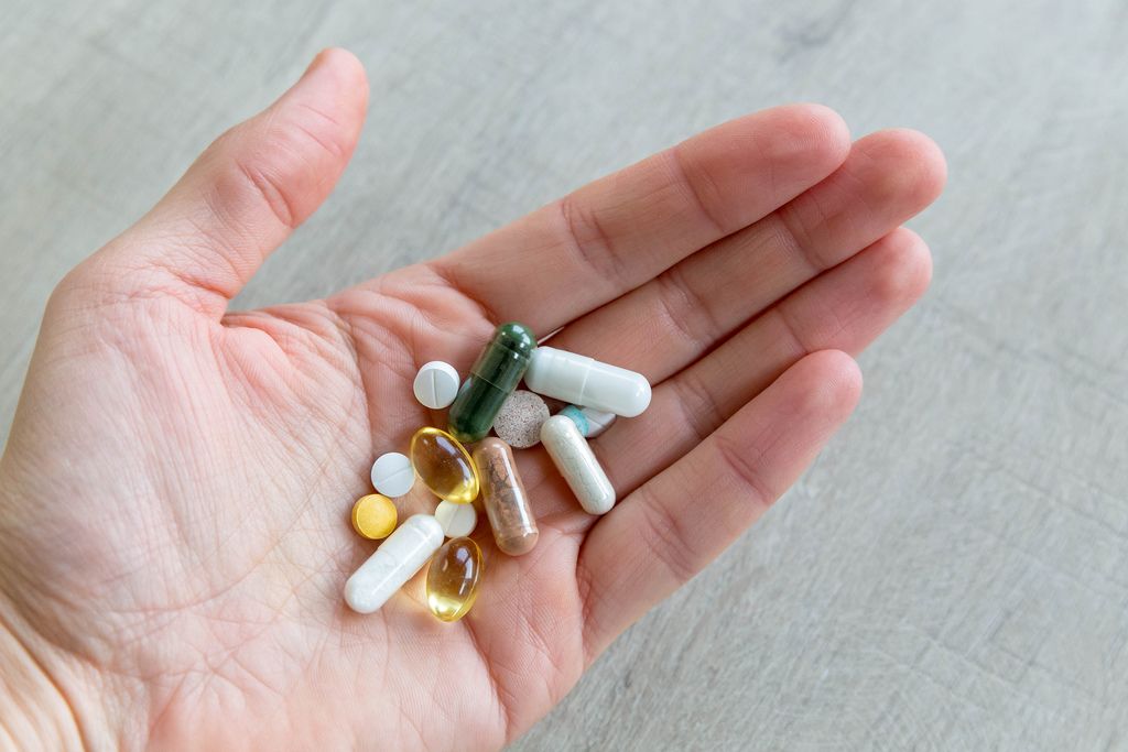 Hand hält verschiedene Tabletten und Vitaminpillen vor grauem Hintergrund