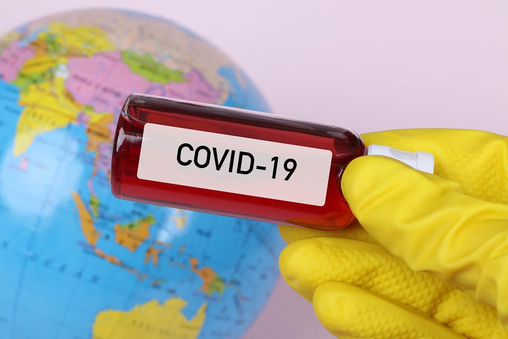 Hand holding blood sample in test tube with COVID-19 text and globe in the background