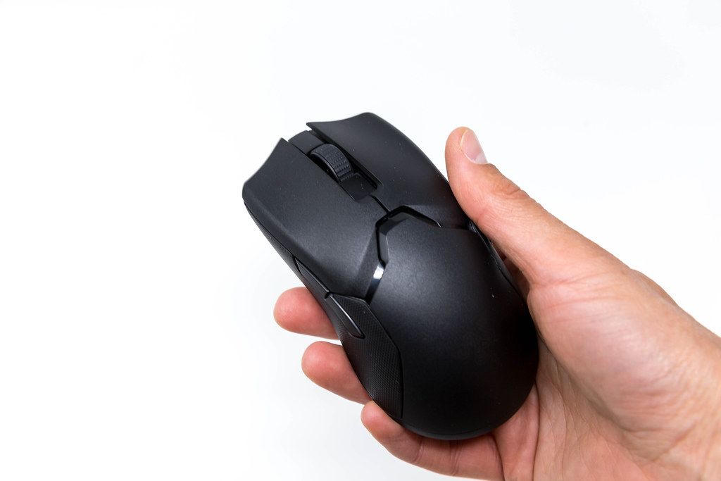 Hand holds the Razer Viper Ultimate wireless gaming mouse in total black version on a white background