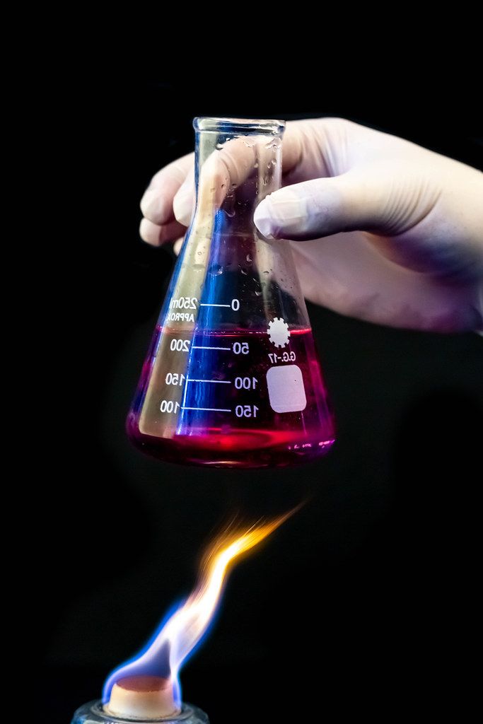 Hand in glove holds flask with chemical solution over fire on black background. (Flip 2020)