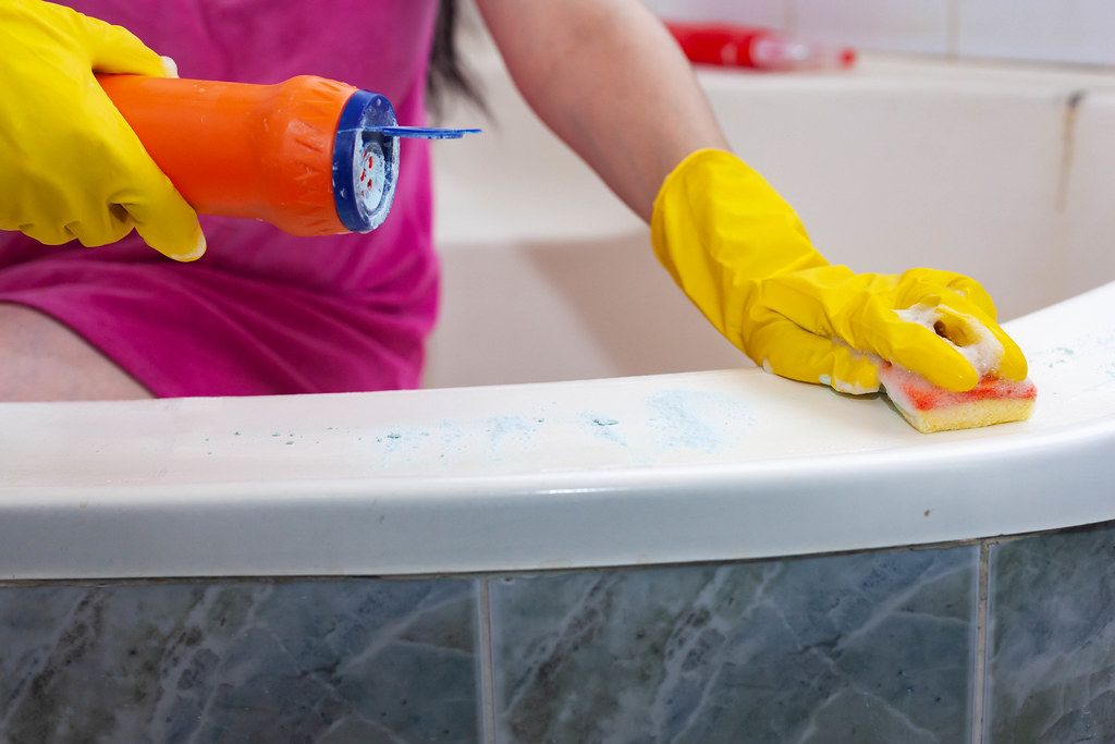 Hand in yellow protective glove cleaning bathtub
