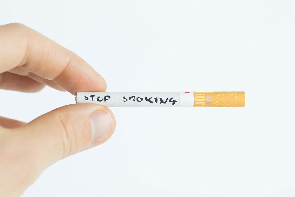 Hand of Person holding a Cigarette with Stop Smoking written on it on white Background