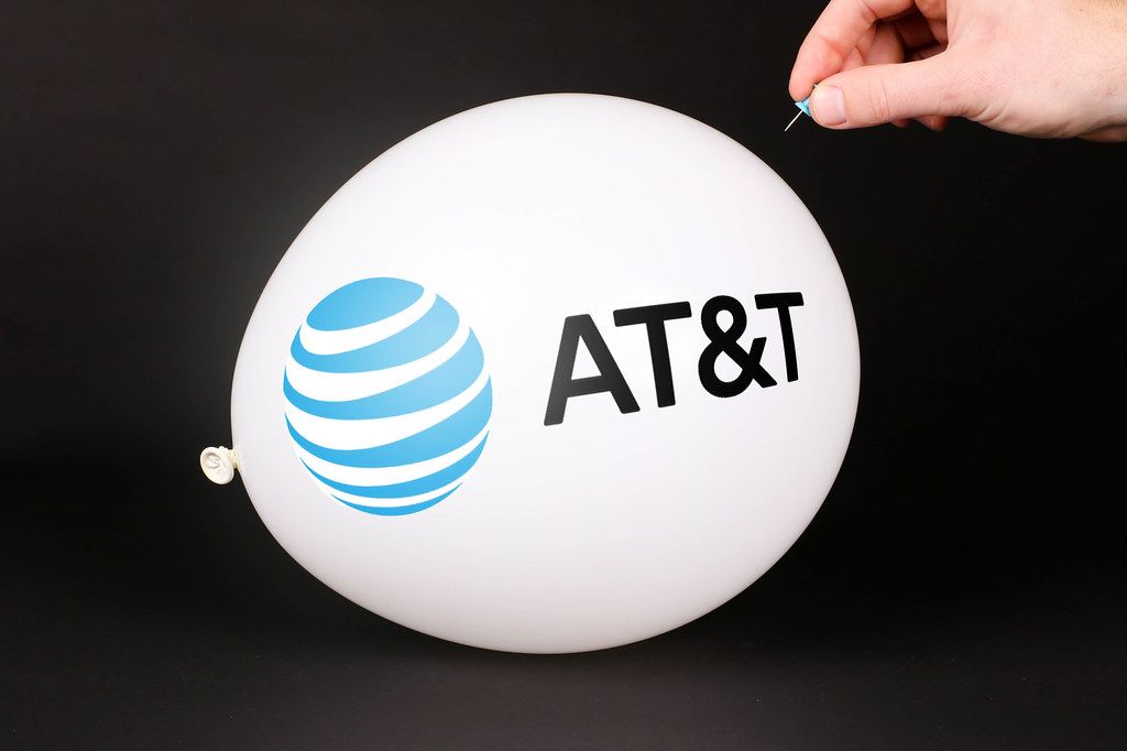 Hand uses a needle to burst a balloon with AT&T logo