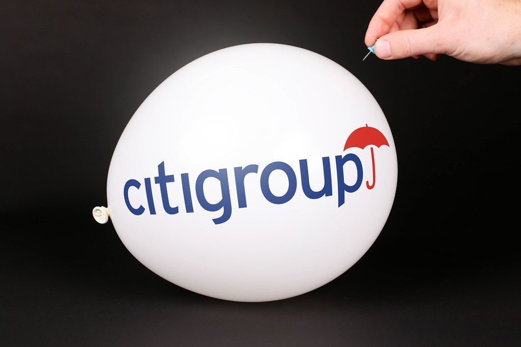Hand uses a needle to burst a balloon with Citigroup logo