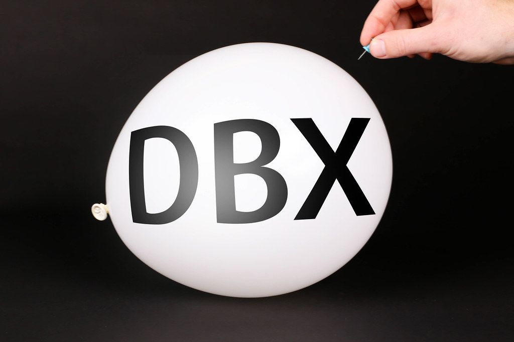 Hand uses a needle to burst a balloon with DBX text