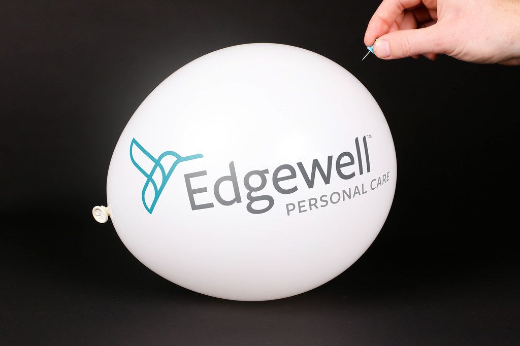 Hand uses a needle to burst a balloon with Edgewell logo