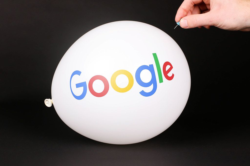 Hand uses a needle to burst a balloon with Google logo
