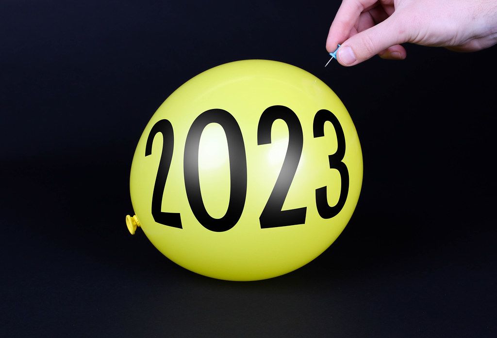 Hand uses a needle to burst a yellow balloon with 2023 text - Creative ...