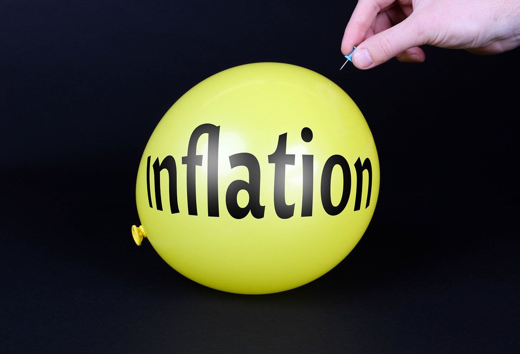 Hand uses a needle to burst a yellow balloon with Inflation text