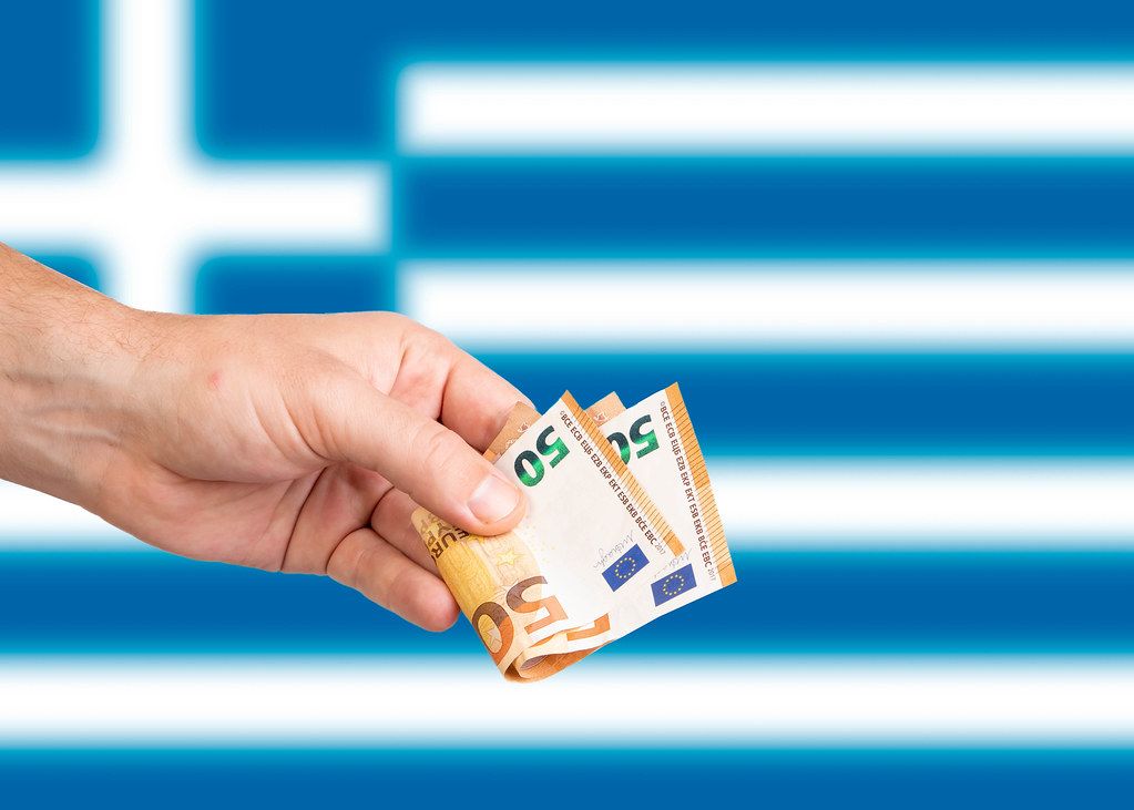Hand with Euro banknotes over flag of Greece