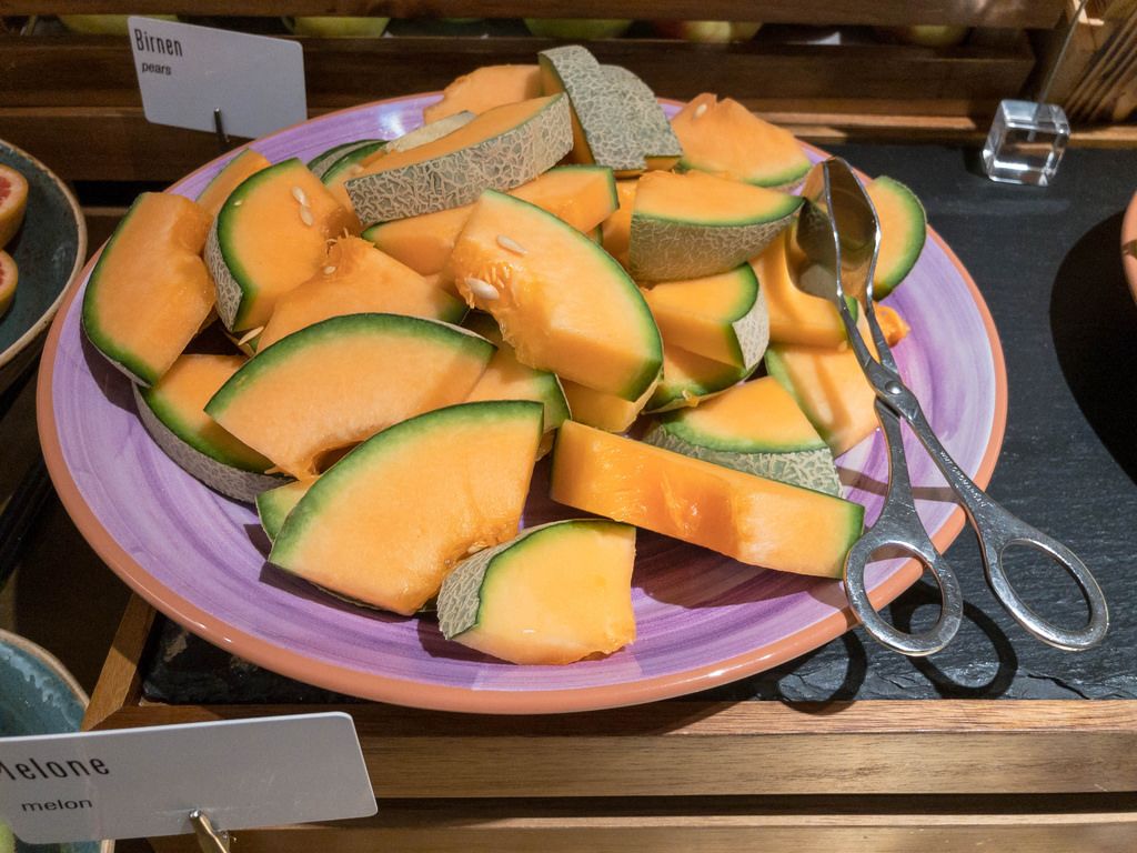 Honigmelonenstücke auf einem Teller zum bedienen mit einer Zange an einem Buffet