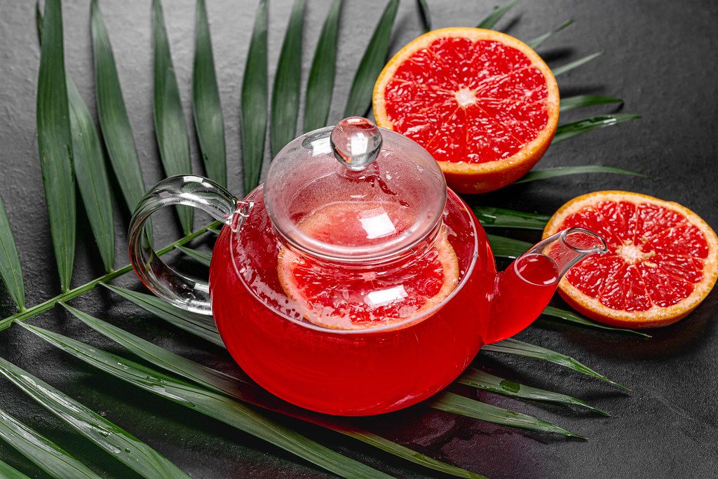 Hot tea with slices of fresh grapefruit on black background with green leaf