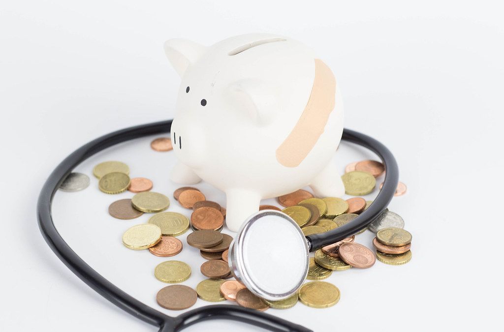 Injured Piggy Bank with Coins and Stethoscope laying next to it on white Background